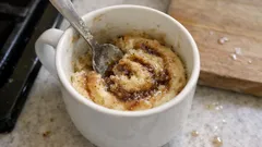 Horký nápoj s pěnou a skořicí v bílém hrnku, míchání lžičkou